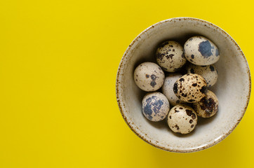 organic quail eggs in bowl on yellow background with copy space.
