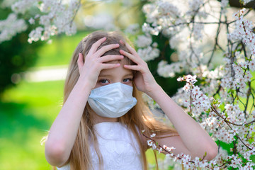 Teenager girl in medical mask in spring flowering garden. Concept of social distance and prevention of coronavirus.