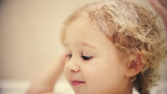 Little blonde baby girl washes her hair with soap