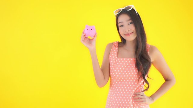 Young pretty woman in a sundress and sunglasses in front of a solid replaceable background raise a  pink piggy bank up for display.