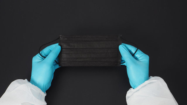 Two Hand Wear PPE Suite And Gloves And Holding Black Face Mask. Put On Black Background.