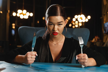 A hungry girl is waiting for food. Holding a knife and fork