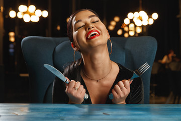 A hungry girl is waiting for food. Holding a knife and fork