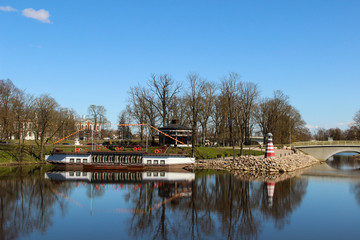 Obraz premium City canal with decorative lighthouse and steam-ship at the coast. Popular waterscape in the city of Jelgava.