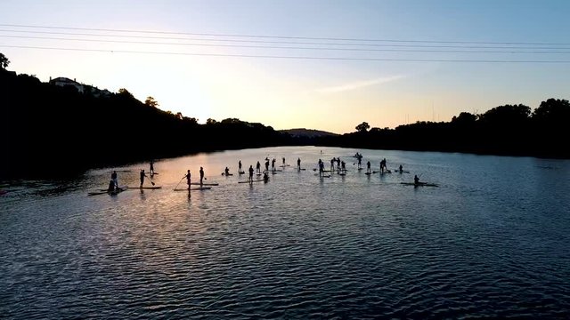 Fly through a group of silhouetted stand up paddle boarders on lake at sunset