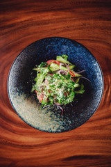Green salad served in dark bowl with wooden background