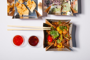 top view of sauces and chopsticks near takeaway boxes with prepared chinese food on white