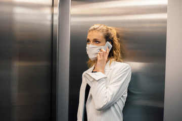 Business woman wearing protective white face mask is using elevator