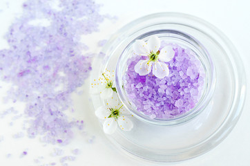 Obraz na płótnie Canvas Small glass bowl with purple bath salt (foot soak) and white flowers. Top view, copy space.