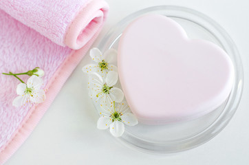 Heart shaped pink bar of soap, pink towel and white flowers. Top view, copy space.