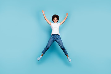 Fototapeta na wymiar Full length photo of funny rejoicing dark skin wavy lady jumping high sunny summer day cheerful good mood wear casual white t-shirt jeans shoes isolated blue color background