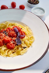 selective focus of delicious pasta with tomatoes served with salt and pepper on white table in sunlight
