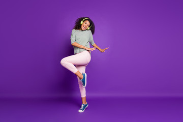 Full length photo of crazy funky brunette hair teen afro american girl have break pause listen song use headset dance dancer wear striped shirt blue pink sneakers isolated violet color background
