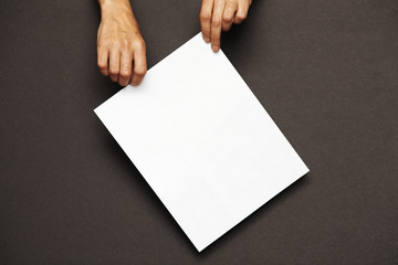 Women's hands hold a sheet of white paper on a dark background