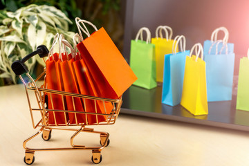online shopping concept. little shopping cart with colorful shopping bags inside  stand near...