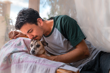 primer plano de hombre joven sentado en un sillon en el jardin bajo una mosquitera, besa la cabeza...