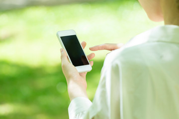 新緑の中でスマートフォンを使う若い女性の手元