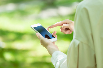 新緑の中でスマートフォンを使う若い女性の手元