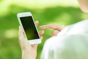 新緑の中でスマートフォンを使う若い女性の手元