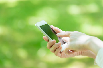 新緑の中でスマートフォンを使う若い女性の手元