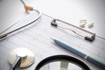 cardiogram with stethoscope, pen, magnifier, pills and glasses lay on a table