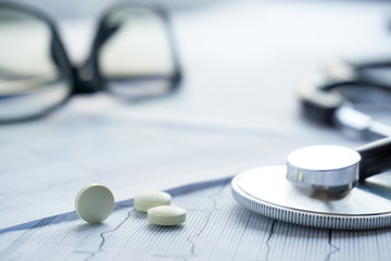 pills with stethoscope, glasses lay on cardiogram. close up