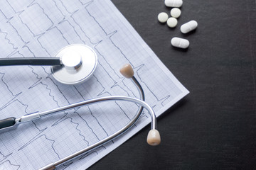 cardiogram with stethoscope, pen, magnifier, pills and glasses lay on a table