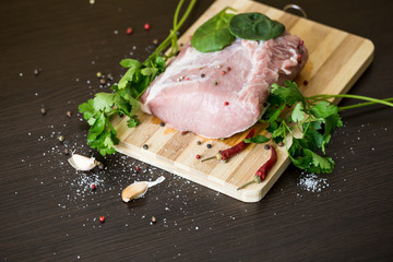 greens, seasonings and meat on a cutting board. a piece of pork, pepper, garlic, salt. Cook at home. fresh food
