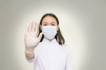 a female doctor in a medical gown and protective mask shows a stop sign, a prohibition sign