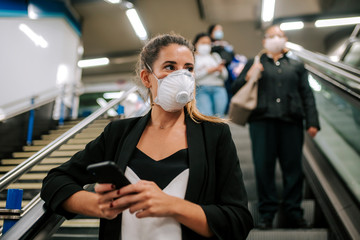 young woman with medical mask in the subway uses her phone