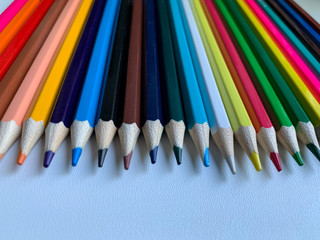 Colored pencils on a white background. Top view of colorful different pencils arranged in a row.