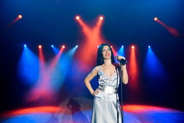 A female singer holding microphone against the colorful lights of the scene. Bright background with neon lights.