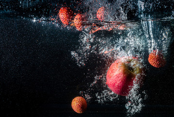 Apple and Lychee berries fall into the water scattering a lot of splashes and drops.