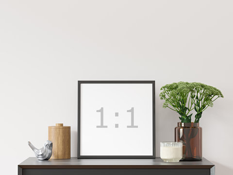 Empty square frame on white wall with black dresser, green plant in brown glass vase and decor - close up image.
