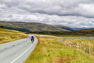 Solo female cyclist cycle through Scottish mountains with her bicycle fully loaded with equipment and camping gear.