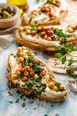 Vegetarian sandwich with addition hummus spread, fresh chopped parsley, chickpeas and olive oil close up view