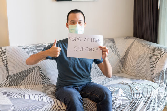 Young Asian man with mask showing Stay At Home sign and giving thumbs up under quarantine
