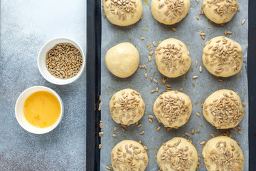 Raw dough balls sprinkled with seeds on pan. Cooking homemade buns. Top view