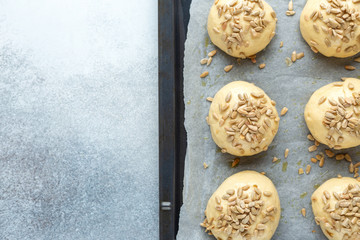 Raw dough balls sprinkled with seeds on pan. Cooking homemade buns. Top view