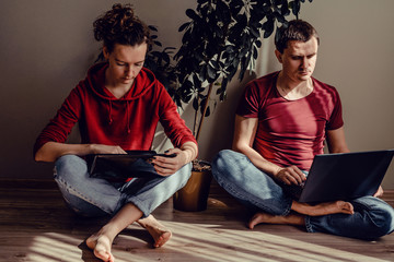 Real modern couple in casual clothes sit on floor use laptops. Woman in red hoodie sweatshirt and jeans with netbook, man in t-shirt bordeaux, denims working on notebook computer. Work at home concept