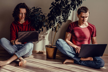 Real modern couple sitting on floor use laptops. Curly headed girl in red hoodie sweatshirt and jeans with netbook, man in t-shirt bordeaux, denims working on notebook computer. Work at home concept