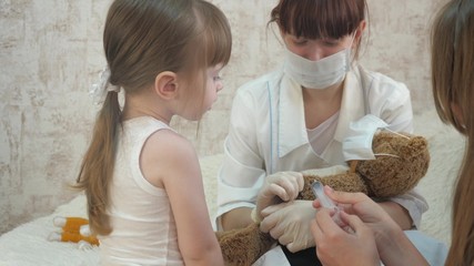 Obraz na płótnie Canvas children play with a medical syringe in protective mask. game pretends to be doctor, nurse, treats patient with vaccine. healthy little girl injects toy bear. child plays in hospital.