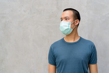 Young Asian man thinking with mask for protection from corona virus outbreak outdoors
