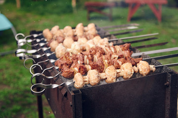 Skewers with meat and mushrooms are laid out on grill