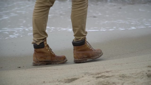Feet in brown shoes walk on the sand on the beach. Woman on the beach. The girl walks large shoes.