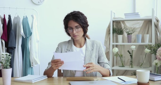 Worried stressed female entrepreneur opening envelope reading bad news in postal mail letter. Upset fashion designer business owner frustrated about bank debt, tax invoice or bankruptcy notification.