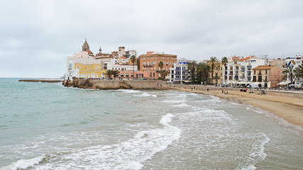 A beautiful beach in Sitges, near Barcelona. Light waves roll onto Spain's Mediterranean beach. Beautiful architecture of Catalonia. Unique landscapes of the Iberian Peninsula