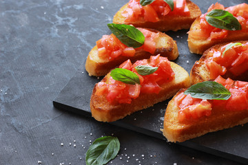Italian appetizer bruschetta with tomatoes and basil on a black board close up.