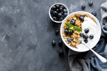 Healthy Breakfast granola with blueberries and yogurt, a glass of milk and berries on a dark background top view