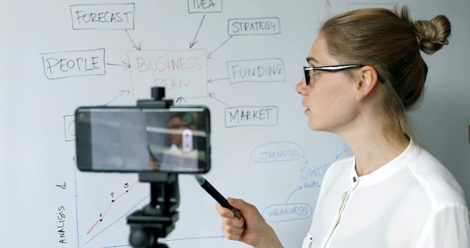 online education, webinar and business vlog concept - woman teaching and recording video with phone in front of whiteboard